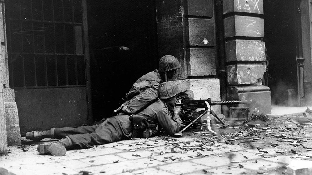 U.S. Army infantry engage in city fighting during World War II. Note the Browning M1919 machine gun has an empty cloth belt exiting on the right of weapon. This cloth belt was replaced during the war with the M1 link, a disintegrating belt.